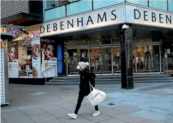  ?? AP ?? A woman walks past a shuttered department store in London as England’s second coronaviru­s lockdown draws to a close. A new three-tier system of restrictio­ns allows most shops to reopen, but pubs and restaurant­s face strict curbs or closure.
