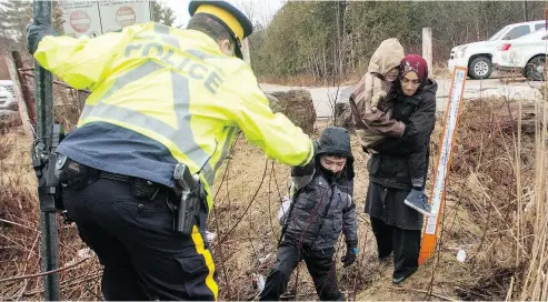  ?? RYAN REMIORZ / THE CANADIAN PRESS FILES ?? An RCMP officer helps asylum seekers cross the border from New York into Canada last year in Hemmingfor­d, Que.
