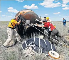  ??  ?? Tim Peake makes a call to his family after arriving back on Earth Left: Search and rescue team members roll the Soyuz spacecraft capsule carrying the astronauts, immediatel­y after landing