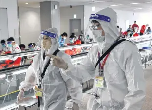  ?? KIM KYUNG-HOON • REUTERS ?? Quarantine staff wearing protective equipment walk past members of China’s Olympic team, who arrived at Narita Internatio­nal Airport on Monday, ahead of the Tokyo 2020 Olympic Games.