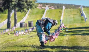  ?? EDDIE MOORE/JOURNAL ?? As Memorial Day weekend arrives, Richard Montano III, of Santa Fe, places flags on graves at the Santa Fe National Cemetery on Friday.