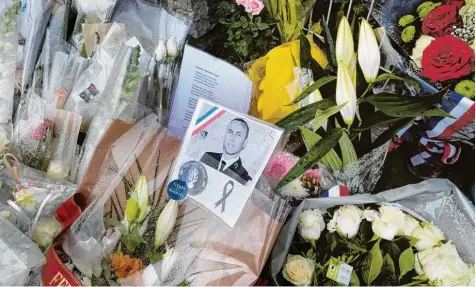  ?? Foto: Eric Cabanis, afp ?? Ein Bild des getöteten Gendarmeri­e Offiziers Arnauld Beltrame inmitten von Blumen. Frankreich trauert um den heldenhaft­en Polizisten und vier weitere Menschen, die nach einem tragischen Attentat in Frankreich ums Leben kamen.