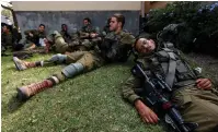  ?? (Amir Cohen/Reuters) ?? WEARY SOLDIERS rest on a patch of grass at Kibbutz Be’eri on Friday after operating in the area following the mass infiltrati­on by Hamas terrorists from the Gaza Strip.