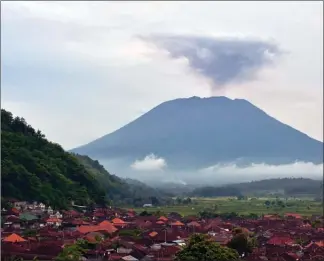  ?? The Associated Press ?? Mount Agung spews volcanic ash into the air behind the village of Bukit Asah, Bali, Indonesia, on Thursday.