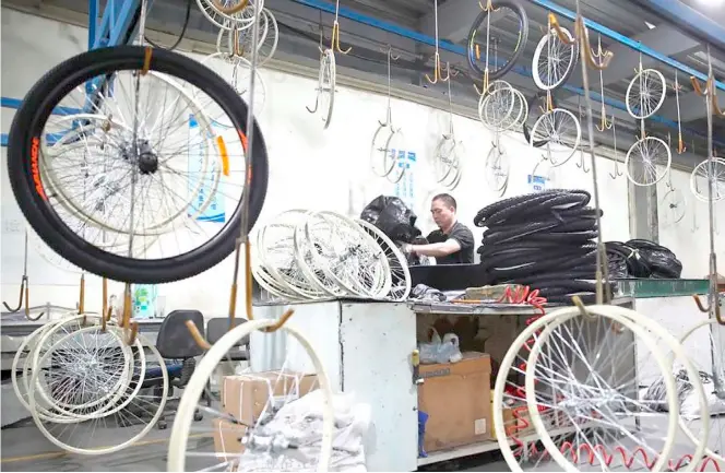  ?? CHINA DAILY ?? A WORKER hauls a set of bicycle wheels at the Golden Wheel Group factory in Tianjin, China. The town was once dubbed as China’s first bike town.