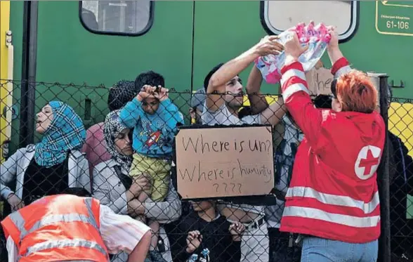  ?? HERBERT P. OCZERET / EFE ?? Miembros de la Cruz Roja reparten botellas de agua a los refugiados que permanecen varados en la estación ferroviari­a húngara de Bicske