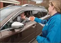  ?? Lori Van Buren / Times Union ?? Volunteer Abby Burke of Saratoga Springs hands a driver COVID-19 tests during a drive-thru event April 27 at Clifton Common in Clifton Park.