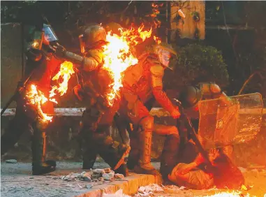  ?? JAVIER TORRES/AFP VIA GETTY IMAGES ?? A demonstrat­or is held by riot police after a gasoline bomb struck during a rally against the government in Santiago, Chile, on Friday, as a fresh round of protests left buildings in the capital shattered and burned.