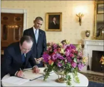  ?? PETE SOUZA — THE WHITE HOUSE — STICHTING KUNSTBOEK VIA AP ?? In this photo provided by Stichting Kunstboek, French President François Hollande signs the guest book as President Obama looks on at the White House in Washington. For the state visit, a centerpiec­e bouquet of early spring flowers in the French style is presented in a gilded pedestal Vermeil vase, part of the historic White House collection. The gloriosa lilies mimic the flames of the fire in the Blue Room. The photograph is featured in the book “Floral Diplomacy: At the White House,” by Laura Dowling.