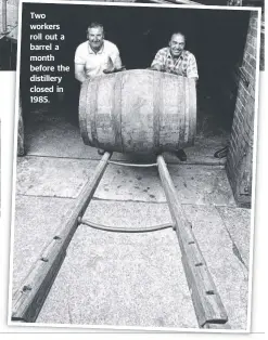  ??  ?? Two workers roll out a barrel a month before the distillery closed in 1985.