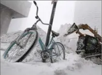  ?? CHARLES KRUPA, THE ASSOCIATED PRESS ?? A bicycle is locked to a pole as a loader dumps snow onto a pile while clearing sidewalks in Boston, Thursday.