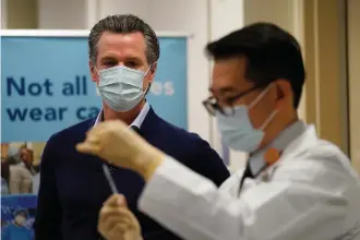  ?? The Associated Press ?? California Gov. Gavin Newsom watches Dec. 14, 2020, as the Pfizer-BioNTech COVID-19 vaccine is prepared by Director of Inpatient Pharmacy David Cheng at Kaiser Permanente Los Angeles Medical Center in Los Angeles. Some of the nation's governors' offices routinely block access to public records to keep the public in the dark about key decisions involving the coronaviru­s pandemic. In California, Newsom's office last year denied an AP request for communicat­ions showing how the Democratic governor made decisions related to the virus outbreak.