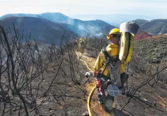  ?? Mike Eliason / Santa Barbara County Fire Department ?? Santa Barbara County firefighte­rs haul dozens of pounds of hose and equipment down steep terrain to extinguish smoldering hot spots in areas hit by the Thomas Fire.