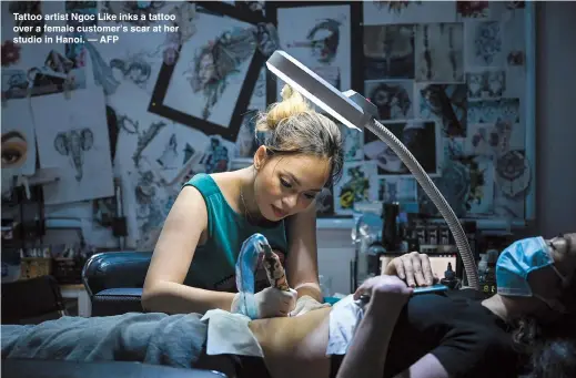  ??  ?? Tattoo artist Ngoc Like inks a tattoo over a female customer's scar at her studio in Hanoi. — AFP