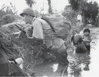  ?? Associated Press ?? n A paratroope­r of the 173rd U.S. Airborne brigade crouches with women and children Jan. 1, 1966, in a muddy canal as intense Viet Cong sniper fire temporaril­y pins down his unit near Bao trai in Vietnam.