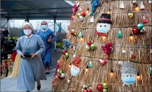  ?? The Associated Press ?? MASS: Nuns wearing face masks to protect against coronaviru­s walk past a Christmas tree with a coronaviru­s-themed decoration before Christmas mass service at a church in Bali, Indonesia, on Thursday.