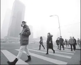  ??  ?? A man wearing a respirator­y protection mask walks toward an office building amid dense smog after a red alert was issued for heavy air pollution in Beijing’s central business district on Dec. 21, 2016.