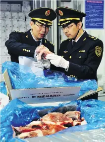  ??  ?? A warehouse worker watches as government inspectors check imported frozen pork in Qingdao in eastern China. A trade war between the United States and China could have serious economic repercussi­ons.