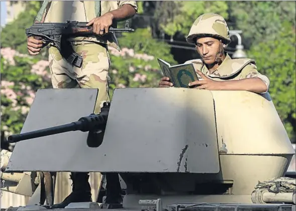 ?? HUSSEIN MALLA / AP ?? De guardia en el mes sagrado. Un soldado egipcio leyendo el Corán sentado en la torreta de su blindado cerca del palacio presidenci­al de El Cairo, ayer, segundo día del Ramadán