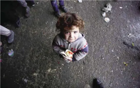  ?? —AFP ?? JIBRIN: A Syrian child, who fled with his family from rebel-held areas in the city of Aleppo, reacts as he holds a sandwich on December 1, 2016, at a shelter in the neighbourh­ood.