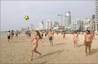  ?? Menahem Kahana AFP/Getty Images ?? BEACHGOERS play soccer in Tel Aviv, whose job market and cultural scene attract many Israelis.