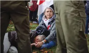  ??  ?? A woman sits with a man lying on the ground near Belarusian law enforcemen­t officers during an opposition rally in Minsk to protest police brutality and to reject the presidenti­al election results.