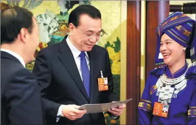  ?? WU ZHIYI / CHINA DAILY ?? Premier Li Keqiang examines photos presented by Wei Zhaohui, a deputy from the Guangxi Zhuang autonomous region (right), on Tuesday. The photos show major changes in Wei’s home village. Li joined a group discussion with the delegation.