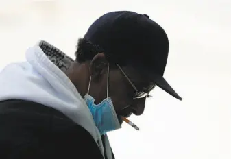  ?? Paul Sancya / Associated Press ?? A smoker lowers his protective mask while puffing a cigarette as he waits for a bus in Detroit. Smoking and vaping both pot and tobacco can weaken lungs and add to the risk of COVID19.