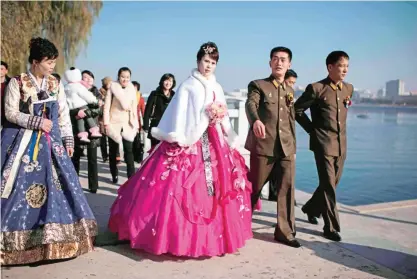  ??  ?? A bride and groom walk with relatives and friends as they prepare to pose for their Wedding photos by the Taedong river in Pyongyang on November 25, 2015. — AFP