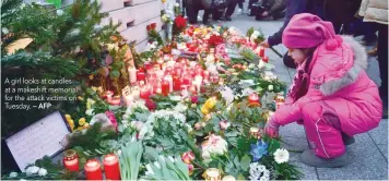  ?? — AFP ?? A girl looks at candles at a makeshift memorial for the attack victims on Tuesday.