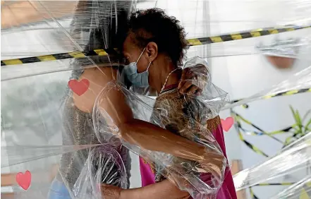  ?? AP ?? Maria Amelia, right, hugs niece Flaviana Silva through a protective plastic barrier during a visit to the Casa Clara home for the elderly in Brasilia. Brazilian President Jair Bolsonaro’s administra­tion is suspending an effort to buy hundreds of millions of syringes, because of high prices, as the country prepares to launch a nationwide vaccinatio­n campaign against Covid-19.