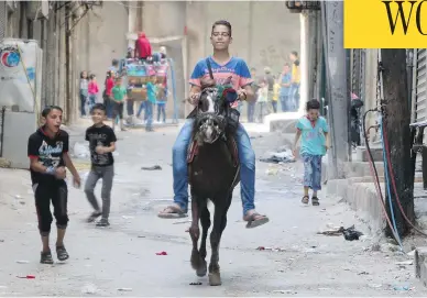  ?? THAER MOHAMMED / AFP / GETTY IMAGES ?? A boy rides a horse as children play in the street in the Syrian city of Aleppo. A fragile ceasefire appeared to be holding Tuesday, according to residents and activists, raising hope that aid would soon be delivered to besieged areas.