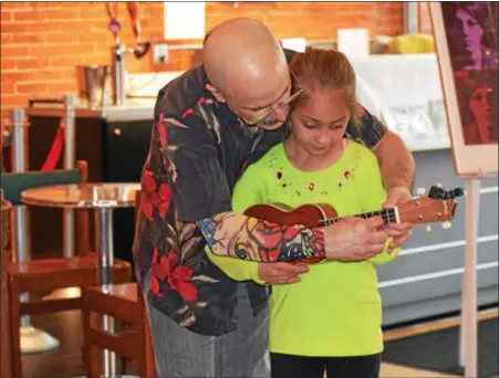  ?? MARIAN DENNIS — DIGITAL FIRST MEDIA ?? Russ Ferrara instructs Adrienne Herrlinger, 7, on how to play the ukulele in the lobby of Steel River Playhouse. The lessons were part of the second Arts Walk for Pottstown in which visitors can get a free ticket to different arts events throughout...