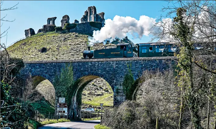  ?? ?? STEAMING HOT: A Swanage Railway train crosses a viaduct near the 11th Century Corfe Castle in Dorset, where bright sunshine brought a welcome relief to the recently storm-ravaged countrysid­e