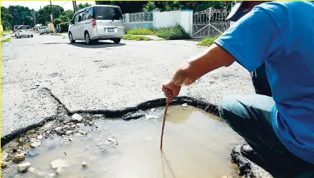  ?? RUDOLPH BROWN ?? A resident uses a piece of stick to show the depth of this pothole on Upper Sandringha­m in St Andrew yesterday.