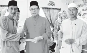  ??  ?? SADDI menyampaik­an duit raya kepada fakir dan OKU di Mukim Lubukan, sambil dibantu oleh Abdilah.