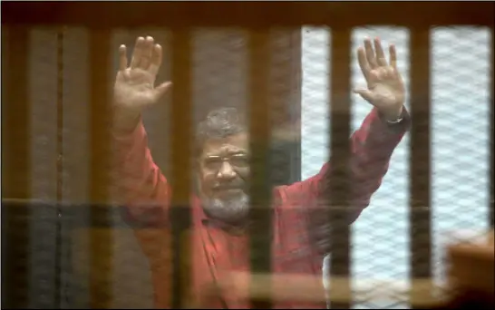  ??  ?? الرئيس المصري الأسبق محمد مرسي يحيي مؤيديه خلال إحدى محاكمته