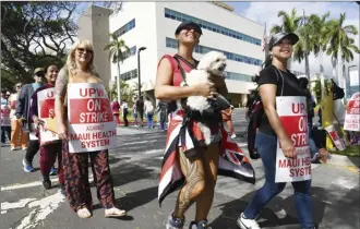  ?? ?? Workers walk the picket line fronting Maui Memorial on Wednesday. Surgery scrub tech Mary Quattrone (center, with dog Bumbo), said on the few days she has off, she picks up shifts valeting cars at the hospital so she can cover her bills each month. “I should be able to cover my rent with one paycheck,” she said.