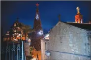  ?? (AP/Oded Balilty) ?? A man walks by a Christmas tree Dec. 12 during the lighting ceremony outside the Greek Orthodox Church of the Annunciati­on in Nazareth, Israel.