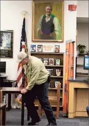  ?? Francine Orr Los Angeles Times ?? ROBERT WALSH moves a table at the library in East Los Angeles. The portrait on the wall of Anthony Quinn was donated by the actor’s family.