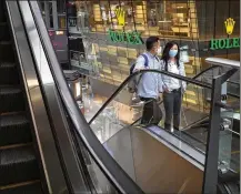  ?? ASSOCIATED PRESS ?? Masked consumers ride an escalator at a shopping mall in Beijing on Friday. China’s virus-battered economy has reopened but job losses have depressed consumer spending.