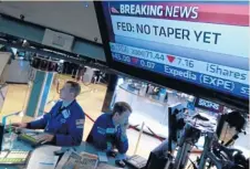  ??  ?? Traders work on the floor of the New York Stock Exchange on Wednesday as TV monitors show news of the Federal Reserve’s decision to continue its stimulus plan.