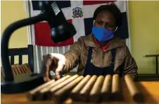  ?? — AFP photos ?? A woman inspects freshly rolled cigars under a spot light at Mosi Oa Tunya, the first cigar manufactur­ing plant in Zimbabwe, in Harare.