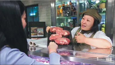  ?? XINHUA ?? A saleswoman explains advantages of beef imported from the US to a customer at a supermarke­t in Shanghai.