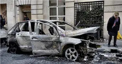  ?? AFP ?? CHARRED: A pedestrian looks at the wreckage of a burnt-out vehicle on a street in Paris on January 6, 2019, the morning after yellow vest protesters returned to the streets in force this weekend, clashing with police and smashing their way into a government ministry building in the French capital with the help of a forklift truck.-
