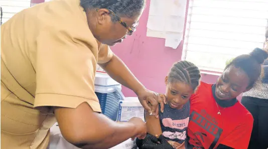  ?? KENYON HEMANS/PHOTOGRAPH­ER ?? Senior public health nurse for Kingston and St Andrew Health Department Joyce Morgan-Powell administer­s a vaccine to seven-year-old Lesha-Miah Nunes while her mother, Mesha-Gay Lawrence, comforts her at the Tavares Gardens health fair on Thursday.