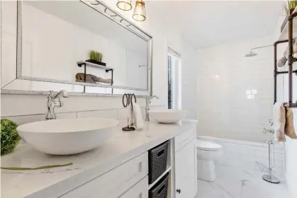  ??  ?? Consistent white finishes capture the main bath on the second level that hosts a dual vanity. Custom pipe and barn wood shelving adds eye-catching, rustic character to accessorie­s.
Bright and accommodat­ing, the generous walk-in closet hosts ample hisand-her capacities with custom shelving, glass jewelry covers, and mirrors.