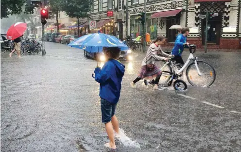  ?? Foto: dpa/Stephanie Pilick ?? Kinder überqueren am Donnerstag eine überflutet­e Kreuzung in Schöneberg.