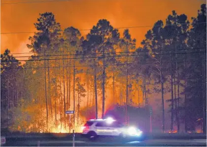  ?? DEVON RAVINE/NORTHWEST FLORIDA DAILY NEWS VIA AP ?? A sheriff ’s vehicle travels along U.S. Route 98 in Walton County, past a hotspot from a wildfire. Authoritie­s say firefighte­rs in the Florida Panhandle battled wildfires through the night and that hundreds of people have been evacuated from their homes.