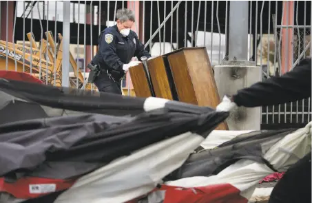  ?? Lea Suzuki / The Chronicle ?? Officer Yvonne Moilanen removes items from a tent at the homeless encampment on the north bank of the Islais Creek Channel.